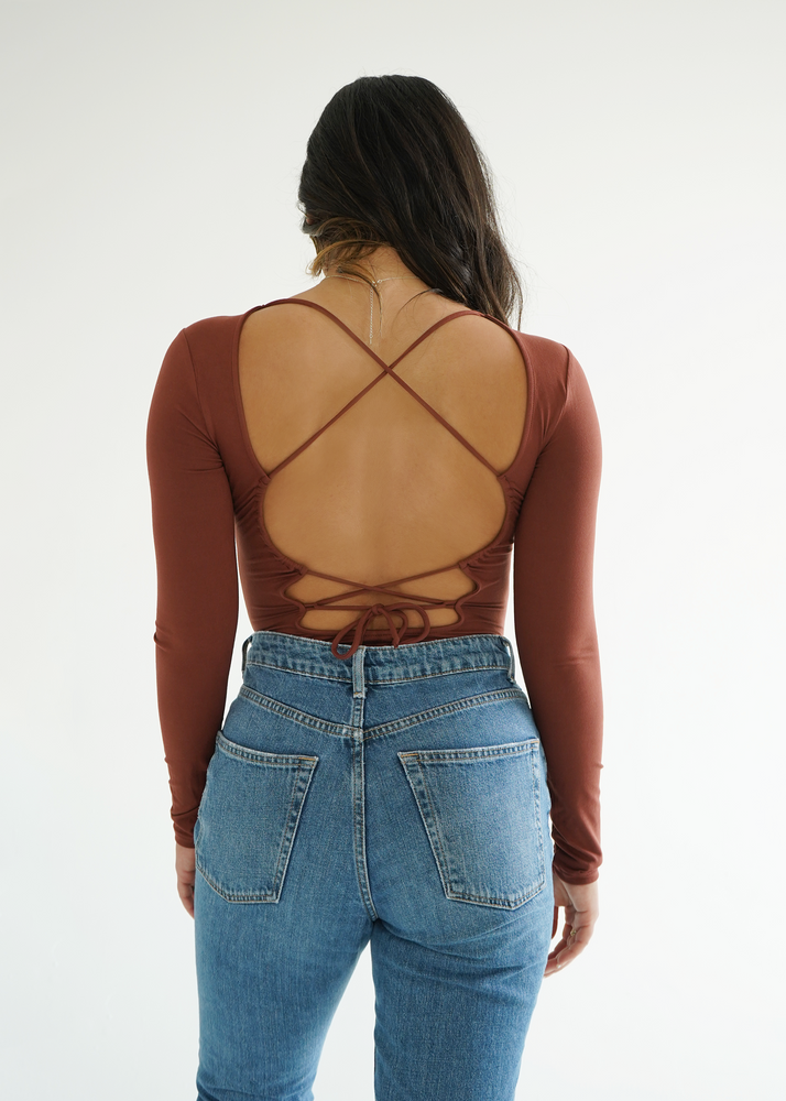 
                  
                    Back view of model wearing the Dani bodysuit with laced details on the back
                  
                